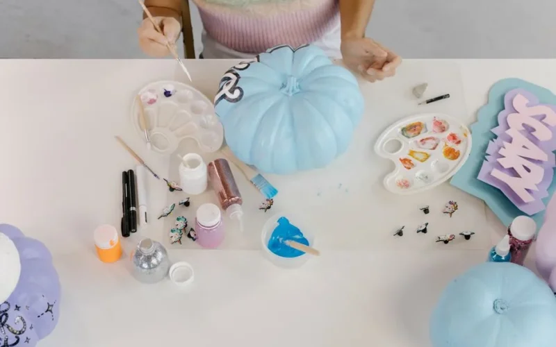 A person painting pumpkins with blue paint for a Halloween decoration.