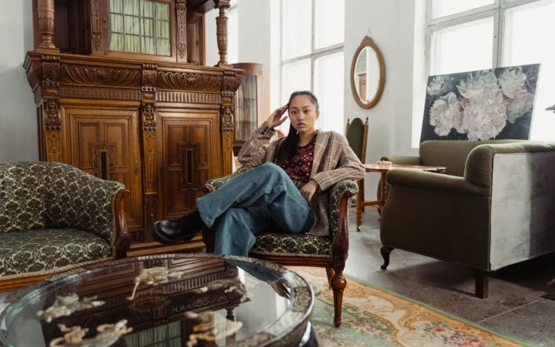 Woman in plaid blazer sitting on vintage sofa in a classic interior setting.
