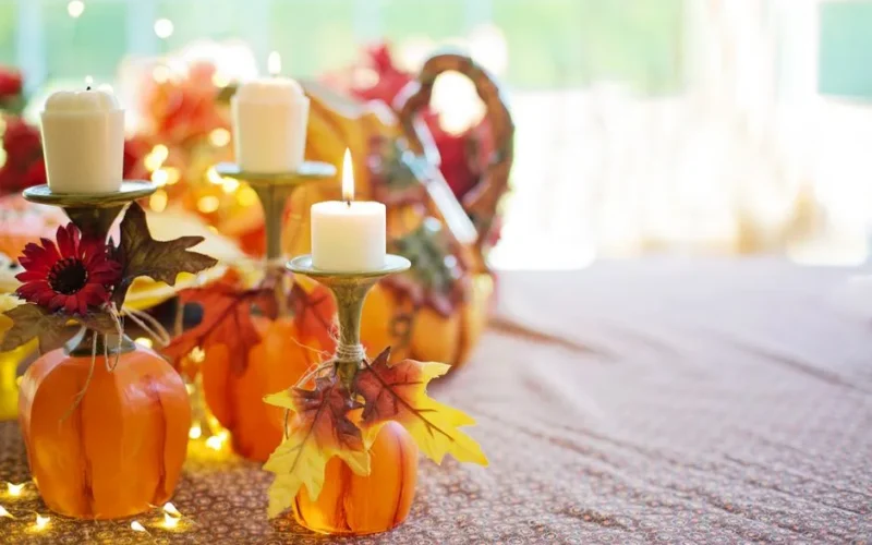 Warm autumn table decor featuring pumpkins, candle holders, and fall leaves.