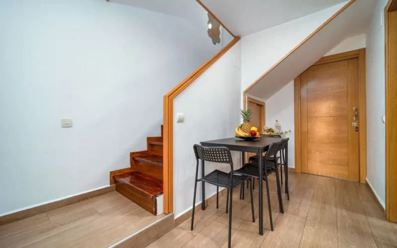 Clean and minimalist interior with wooden accents, featuring a small dining area under the stairs.