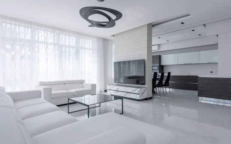 Interior of light apartment with table and couch near TV with cabinet and white walls near window with curtains and stool near lamp