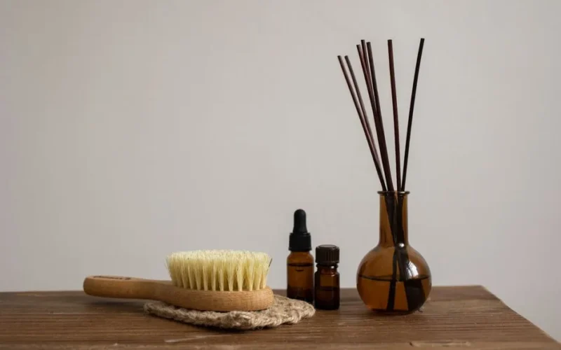 Minimalist aromatherapy set with essential oils, brush, and diffuser sticks on wooden table.