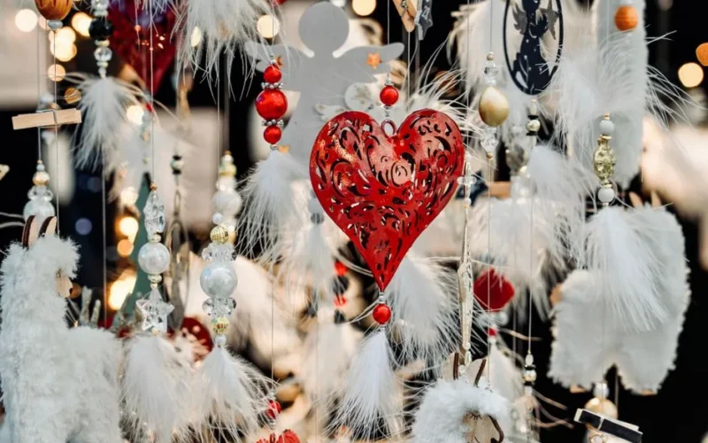 A vibrant display of holiday decorations featuring a red heart ornament surrounded by white feathers and lights.