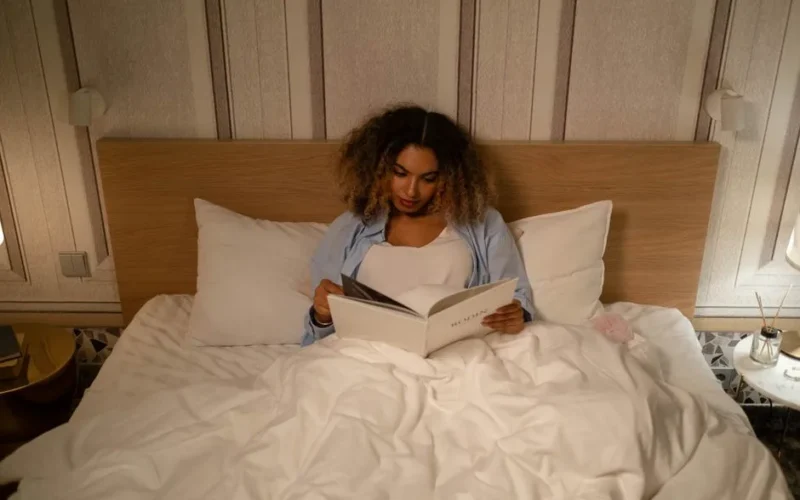 African American woman enjoys a peaceful evening reading in bed, capturing a moment of leisure and relaxation.