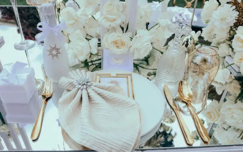 A beautifully arranged outdoor table setting featuring white roses, fine glassware, and gold cutlery.