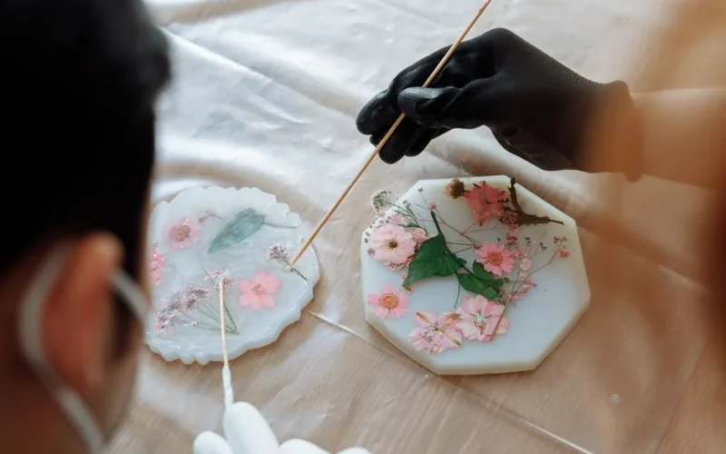 Close-up of hands arranging dried flowers in resin molds for decorative art.