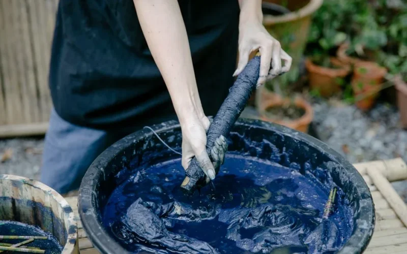 A close-up of hands dyeing fabric with indigo dye outdoors, emphasizing traditional techniques.