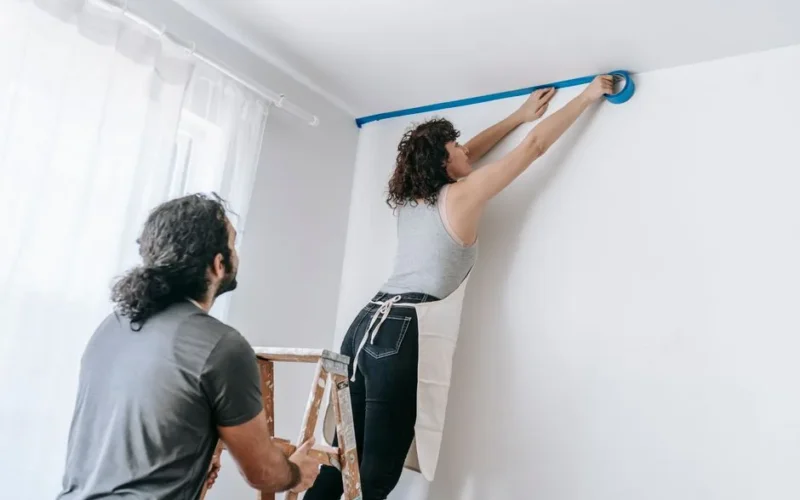 A couple collaborates to tape and paint a room during a home improvement project.