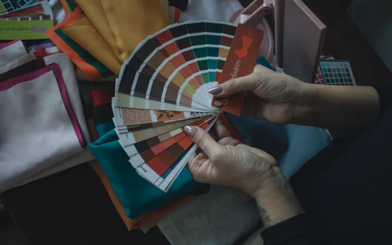 Hands holding color swatch above fabrics. Ideal for design, fashion, and color theory themes.