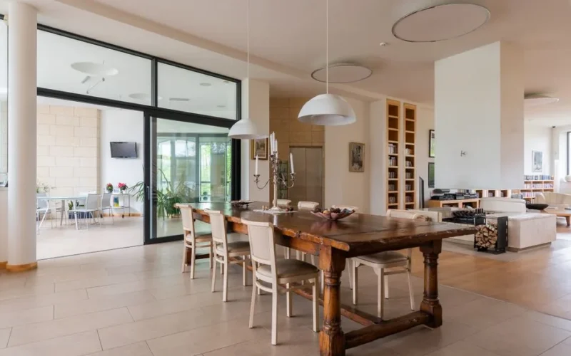 Wooden table with candlestick and chairs placed near modern living room in stylish apartment with hanging lamps against doorway overlooking terrace