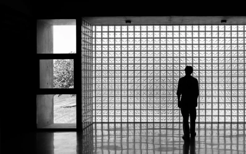 A lone figure stands in silhouette against an illuminated glass block wall, creating a moody and artistic scene.