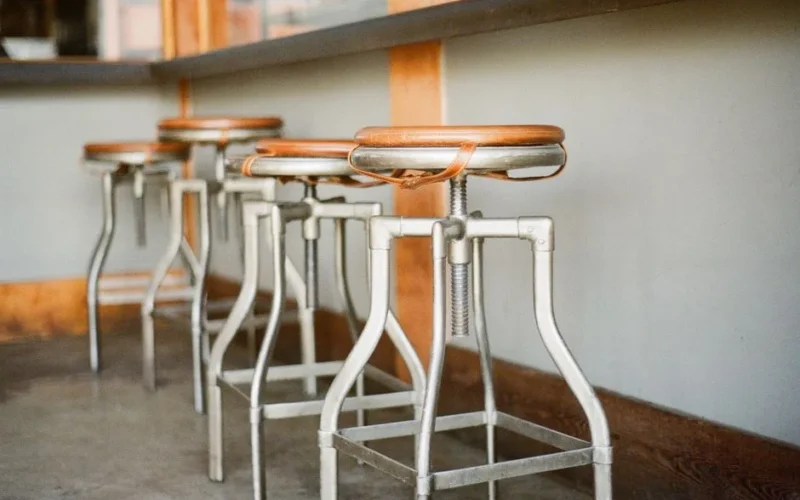 Industrial bar stools with wooden seats lined up in a rustic indoor setting.