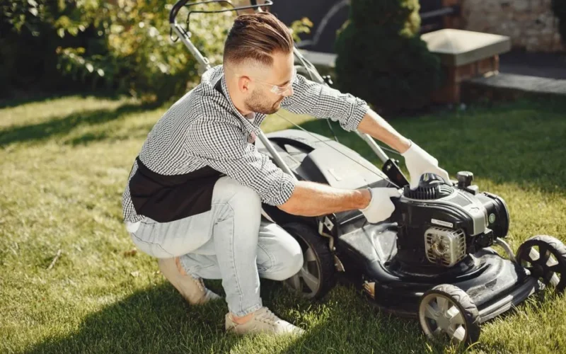 Man preparing lawn mower for garden work on a sunny day outdoors.