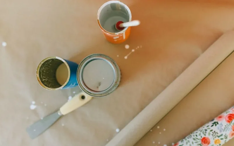Top view of paint cans, scraper, and wrapping paper on a brown surface.