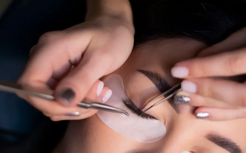 Detailed view of a beautician applying eyelash extensions to a woman's eyes.