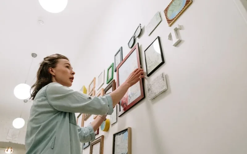 A woman arranging picture frames on a bright indoor wall.