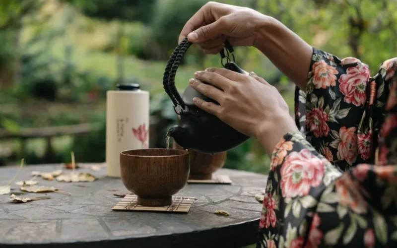 Hands pouring tea during a traditional Japanese tea ceremony in a peaceful garden setting.