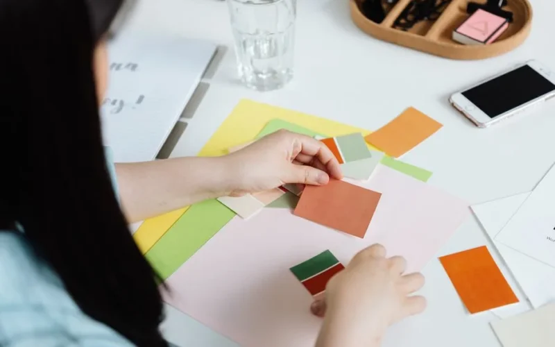 An interior designer arranging color swatches on a desk with a smartphone nearby.