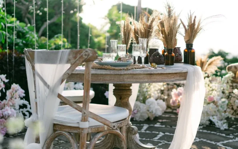 Elegant outdoor table setting with rustic decor, pampas grass, and flowers, perfect for a wedding or special event.