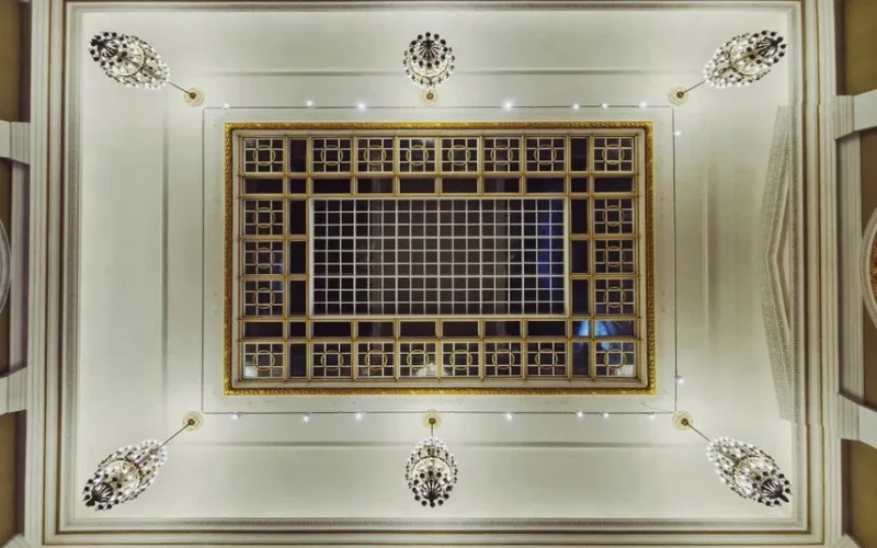 Elegant view from below of an ornate ceiling featuring chandeliers and a gold-accented grid design.