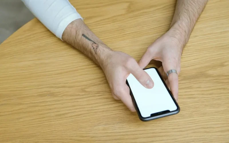 Close-up of hands using a smartphone with a blank screen on a wooden table indoors.