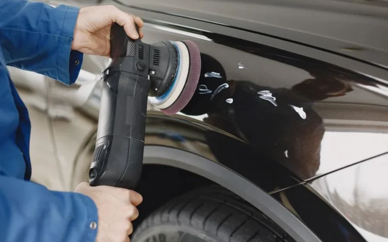 Hands using a polishing machine on a car's surface in a garage setting.