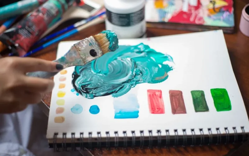 Close-up of a person mixing vibrant paints with a brush on paper. Artistic inspiration in action.