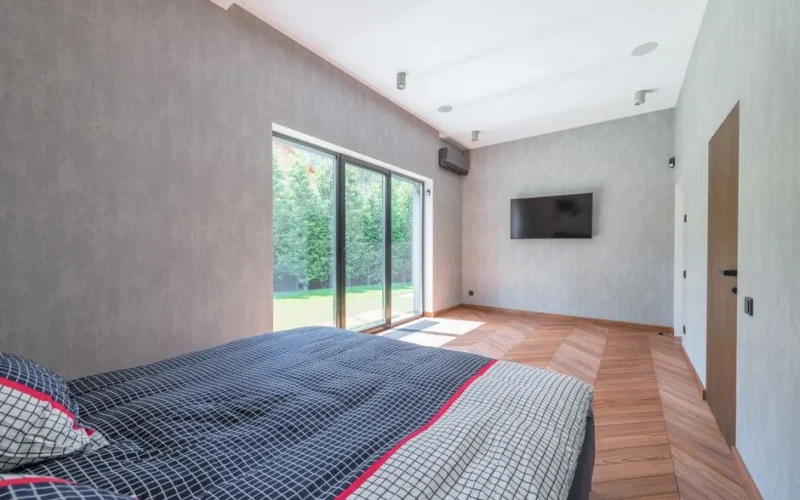 Bright and cozy minimalist bedroom with large sliding glass doors and wooden flooring.