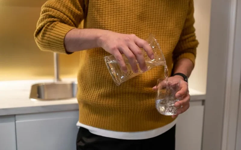 Close-up of individual pouring water into glass in a modern kitchen.