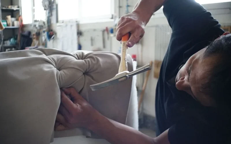 Skilled artisan working meticulously on a sofa using upholstery tools in a workshop.