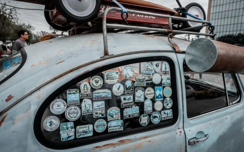 Close-up of vintage car window covered in various travel stickers, showcasing retro vibes.