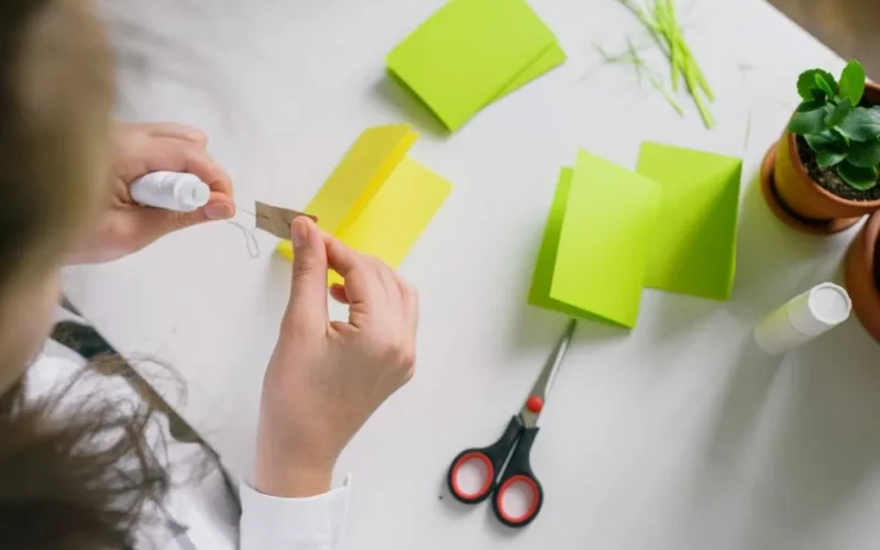 A person engaged in crafting, folding vibrant papers with tools on a desk.