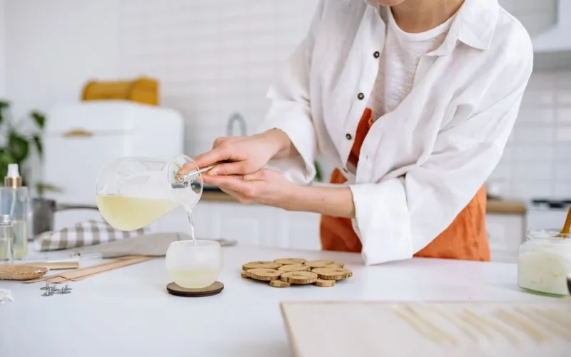 A craftswoman pouring wax into a candle mold in a cozy kitchen. Perfect for DIY and crafting themes.