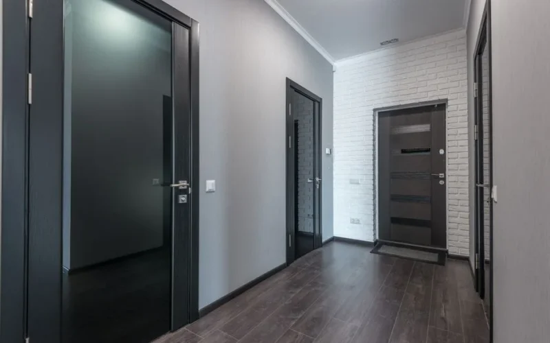 Interior of empty spacious corridor with laminate floor and black doors with glass parts and white ceiling and gray painted walls