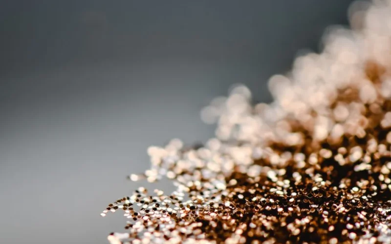 A close-up photograph capturing the shimmering beauty of gold glitters against a gray background.
