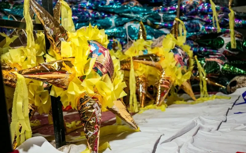 Colorful star-shaped Mexican piñatas with decorative yellow paper in a vibrant market setting.