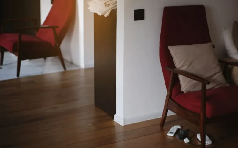 Stylish red armchair with wooden legs in a warm, minimalist living room setting.