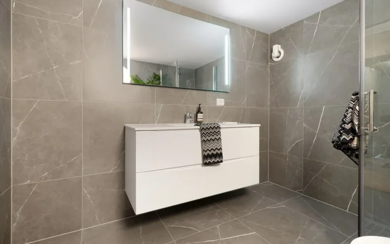 Elegant bathroom featuring a large mirror, modern vanity, and sleek grey tiled walls.
