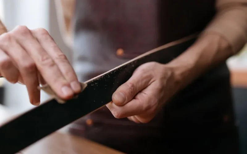 Close-up of hands sanding a wooden strip with sandpaper in a workshop setting.
