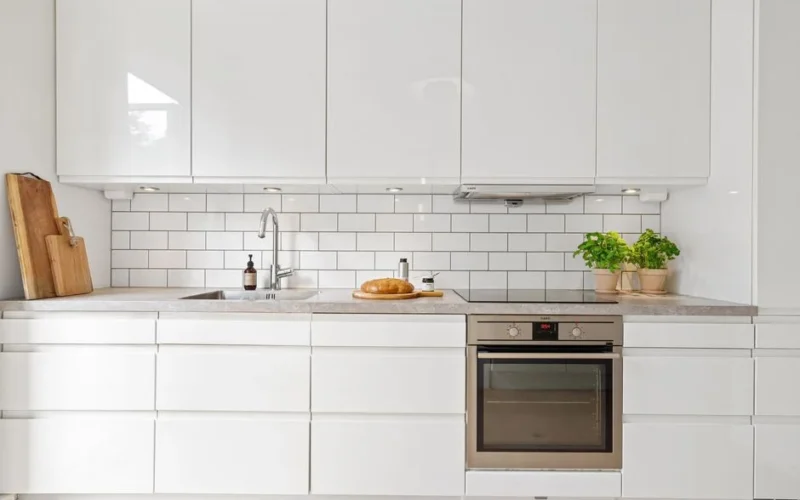 Sleek white kitchen featuring subway tiles, built-in oven, herbs, and bread for a modern touch.