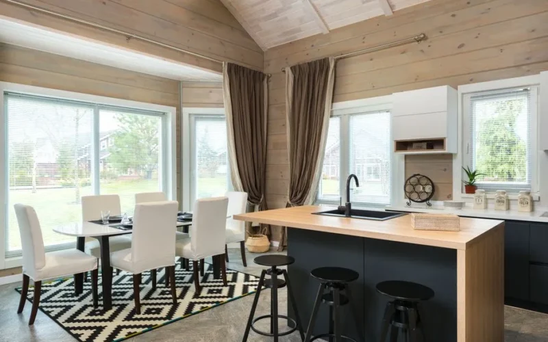 Contemporary convenient kitchen with bar chairs at counter near dining table and chairs on carpet in suburb house with panoramic windows