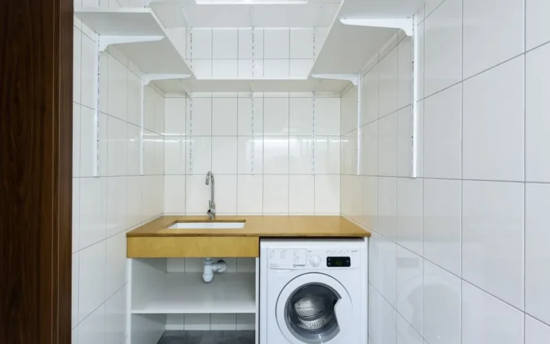 Modern laundry area with white tiled walls, washing machine, and built-in shelves.