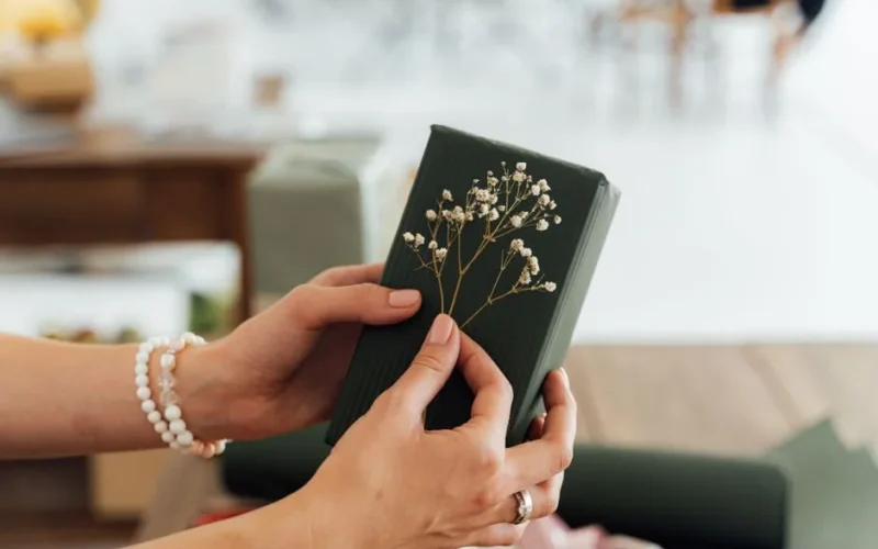 Close-up of hands holding a beautifully wrapped gift with floral accents, ideal for special occasions.