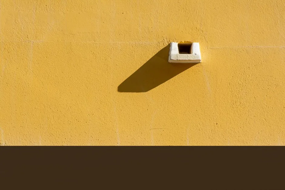 Close-up of a yellow painted wall with a sharp shadow, creating a minimalist urban aesthetic.