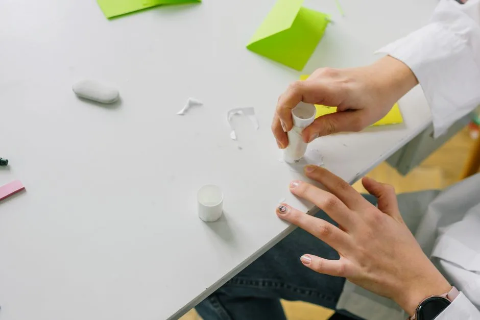 Close-up of hands applying glue stick on paper for a craft project on a desk.