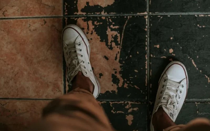Top-down view of white sneakers on an aged tiled floor, displaying casual fashion against a rustic background.