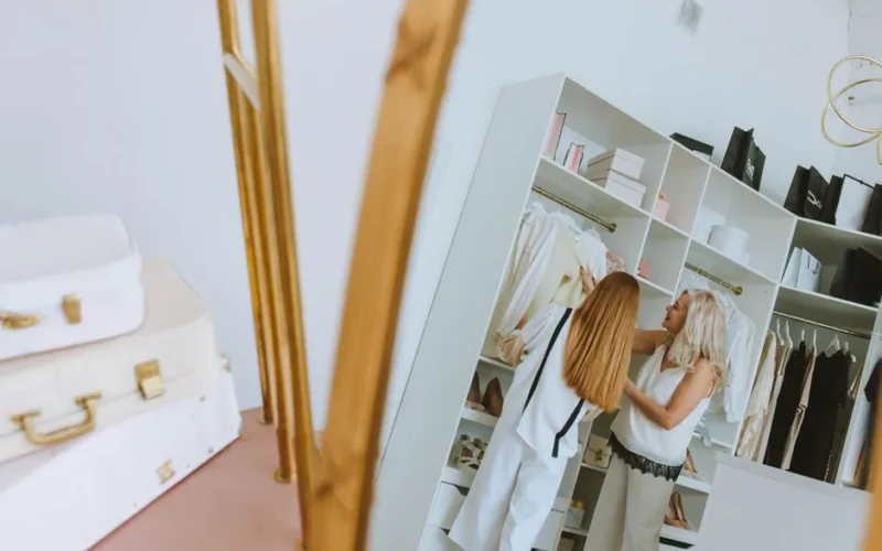 Two women selecting clothes from a stylish wardrobe in a chic room setting.