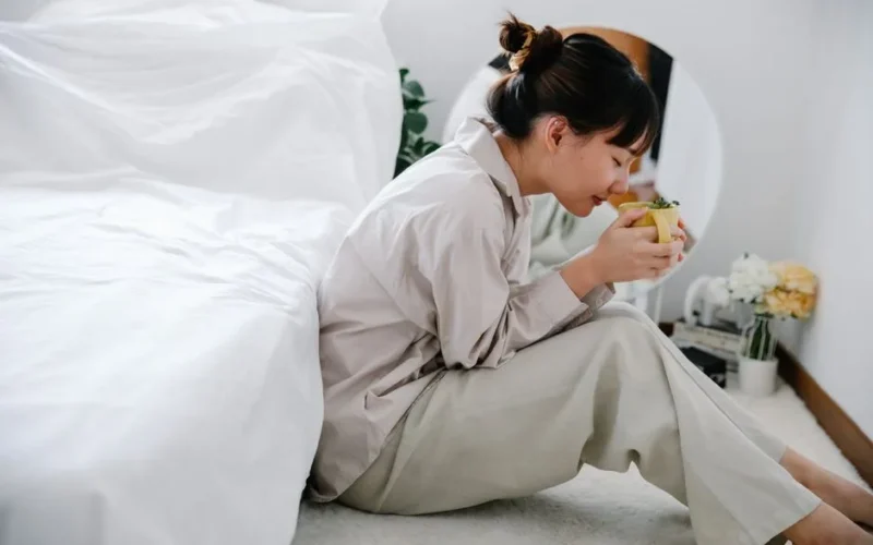 Woman enjoying a warm herbal tea while relaxing in a cozy bedroom setting, capturing a serene morning vibe.