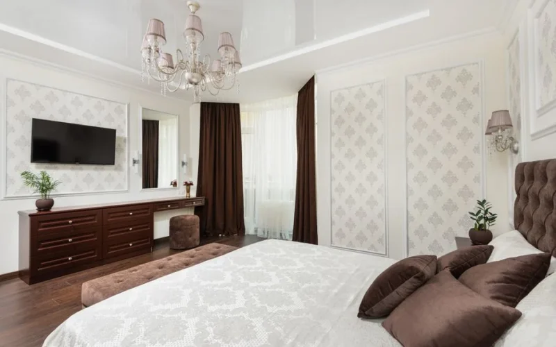 Spacious bedroom featuring luxurious design elements like plush pillows, chandelier, and dresser.