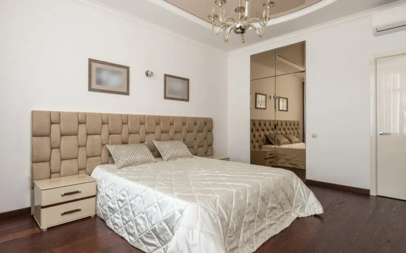 Stylish modern bedroom with plush headboard, chandelier, and mirrored closet doors.